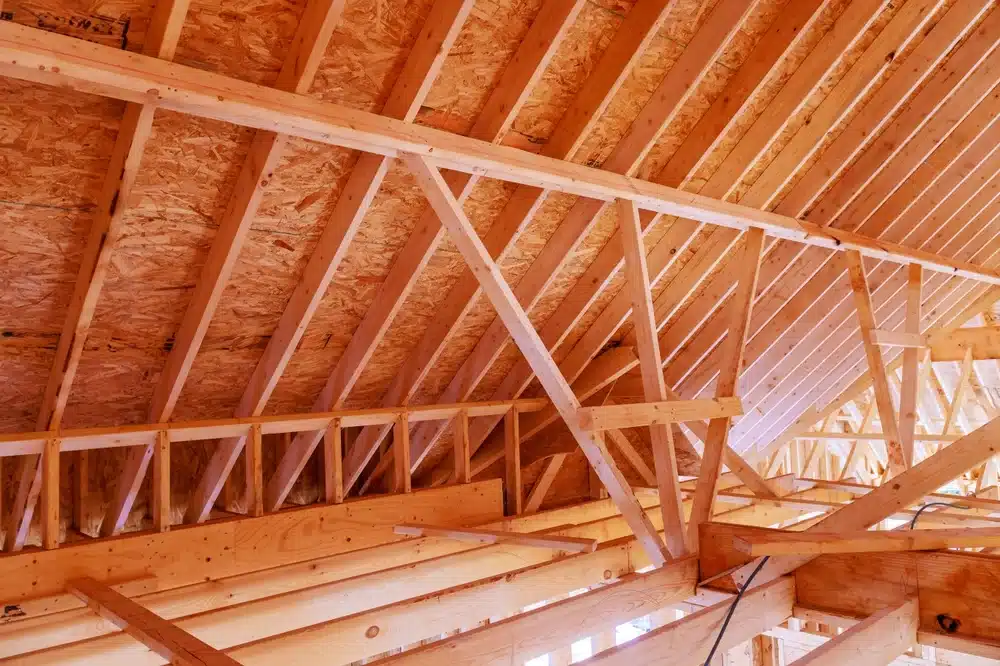 Des fermes de toiture en bois forment un motif triangulaire dans un bâtiment en construction. Le bois clair évoque une sensation de chaleur et un potentiel encore inexploité.