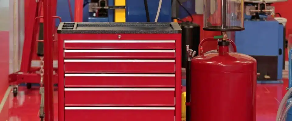 Une servante d'atelier rouge à plusieurs tiroirs se trouve dans un atelier. À ses côtés, un cylindre rouge et diverses machines bleues créent une atmosphère industrielle et ordonnée.