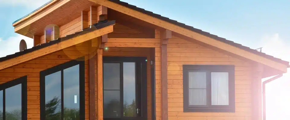 Un chalet en bois moderne doté de grandes baies vitrées et d'un toit en pente. La lumière du soleil éclaire doucement la scène, créant une atmosphère chaleureuse et accueillante.